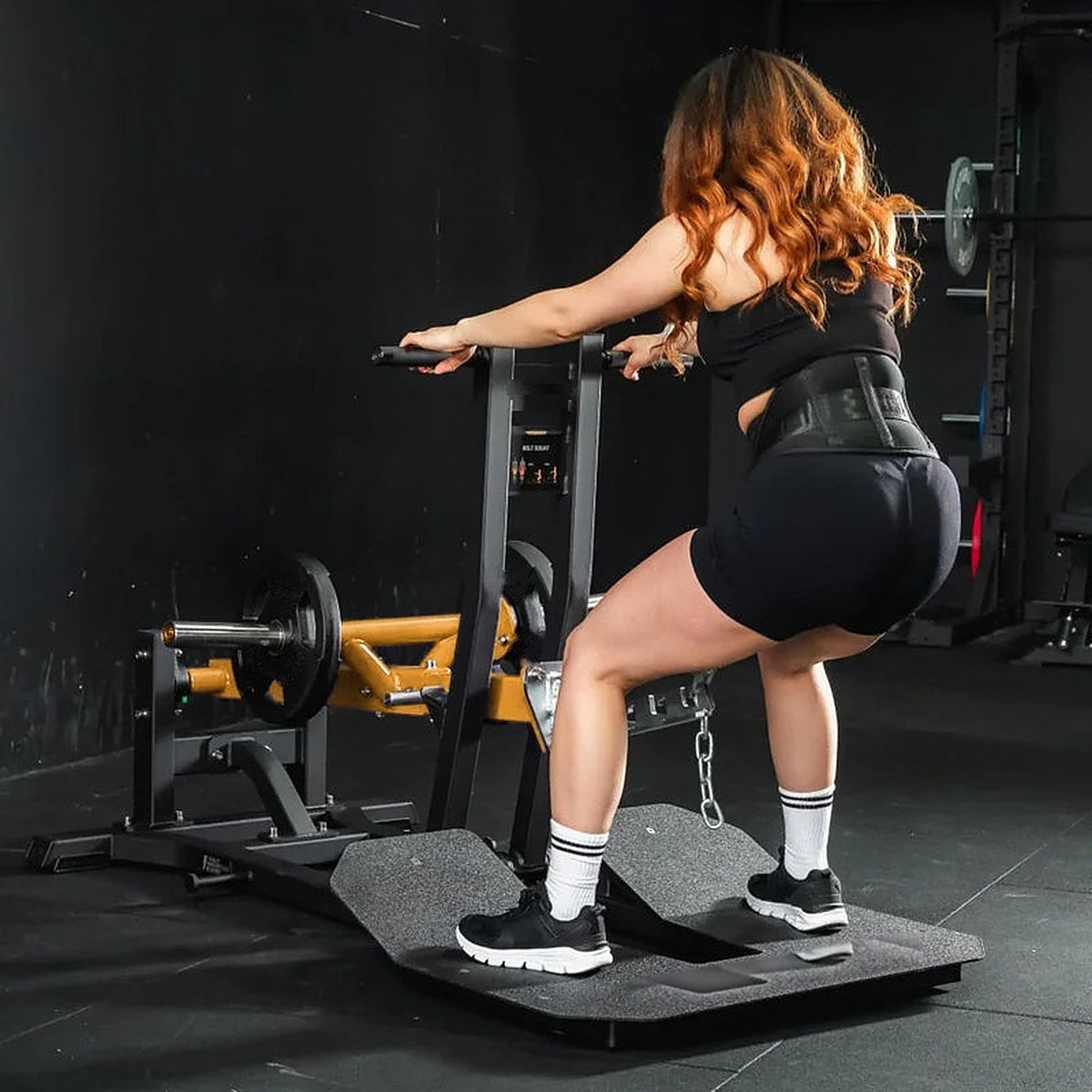 Femme en belt squat sur la machine UltraFitness jaune, ceinture de lest à la chaîne